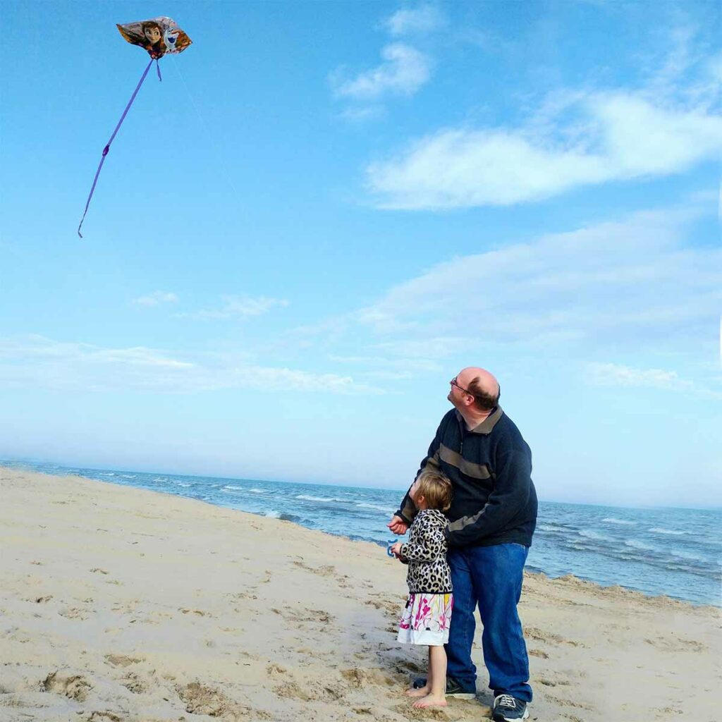 dad and daughter flying a kite on the beach