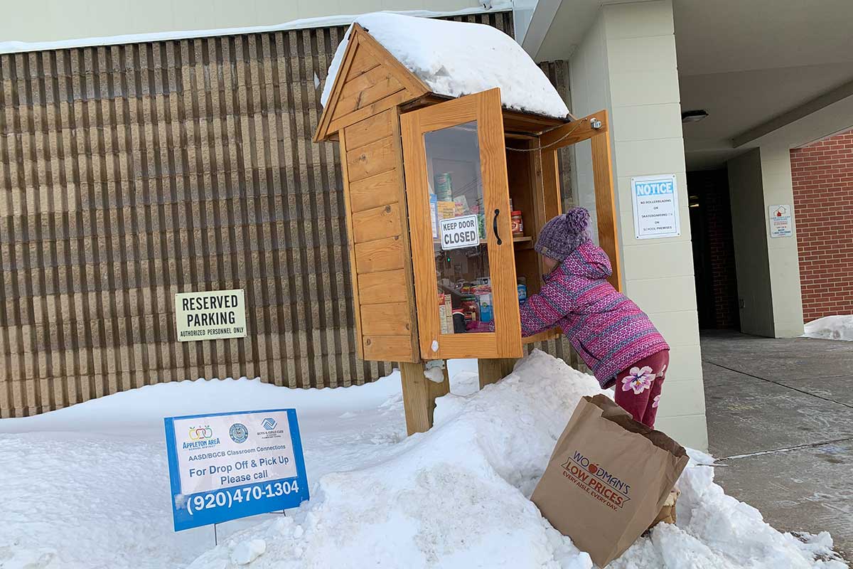 child adding books and food to Little Free Pantry in Appleton