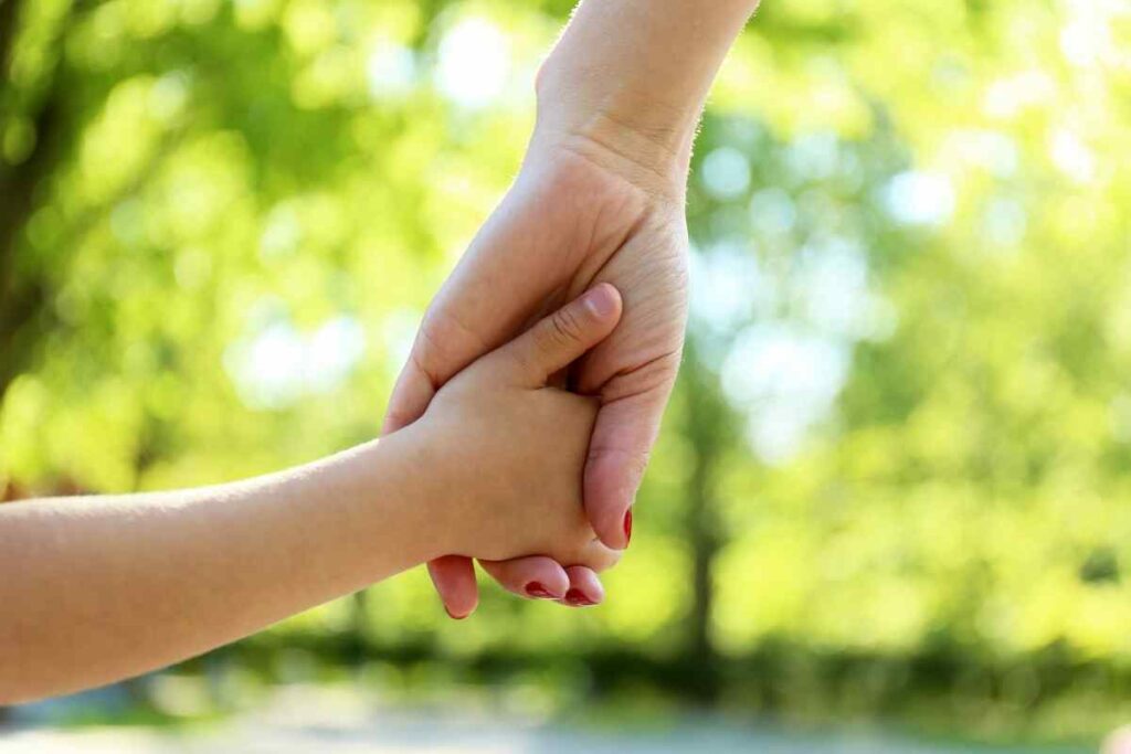 adult with red nail polish holding the hand of a child